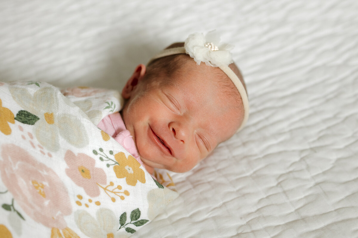 Longmont CO newborn smiling while laying on bed swaddled