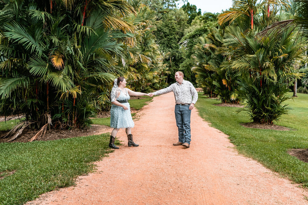 woman in blue dress and man in jeans and dress shirt dancing on a dirt path in a Townsville botanical garden - Townsville Engagement Photography by Jamie Simmons
