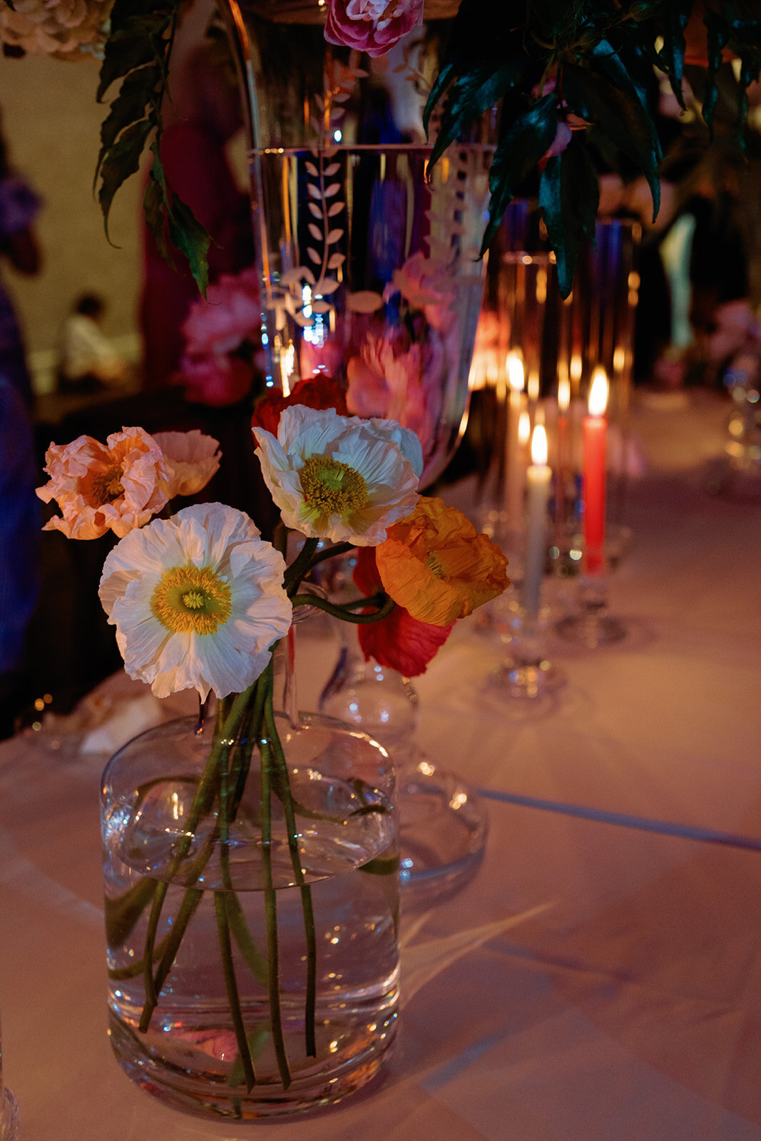 Close-up of colorful poppy flowers in a glass vase surrounded by glowing candlelight during Callie & Hayes’ wedding reception at Burritt on the Mountain.