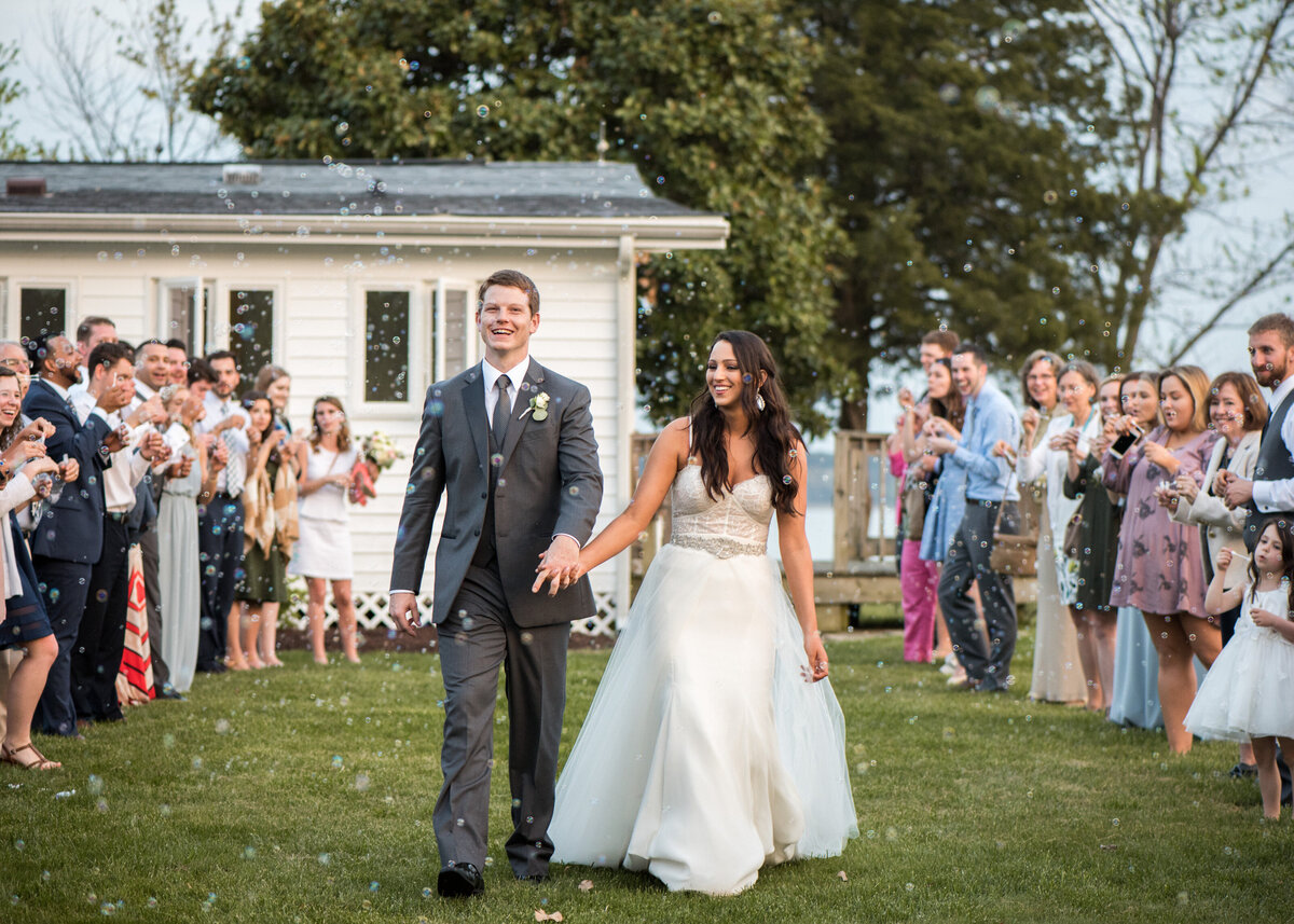 Newlyweds walking through a tunnel of their guests as they blow bubbles towards them 