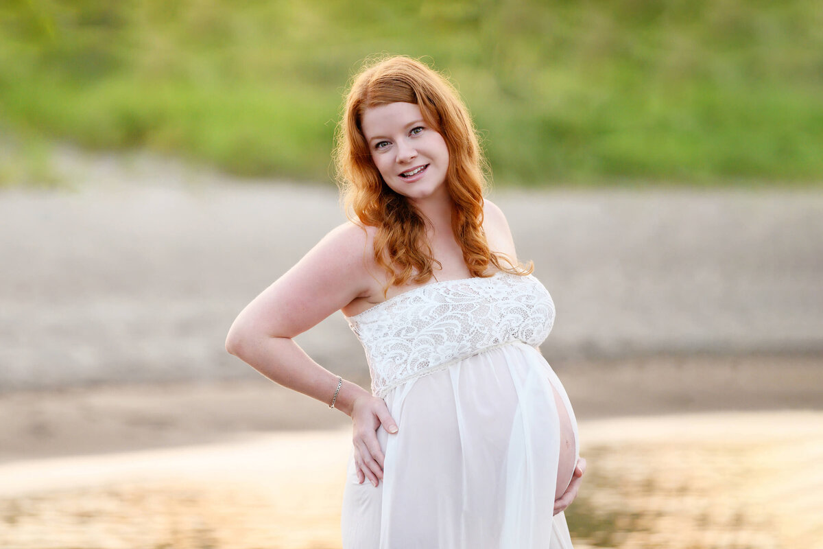 pregnant woman standing in the water with the sunsetting behind her for her outdoor beach maternity photography session in Burlington, On