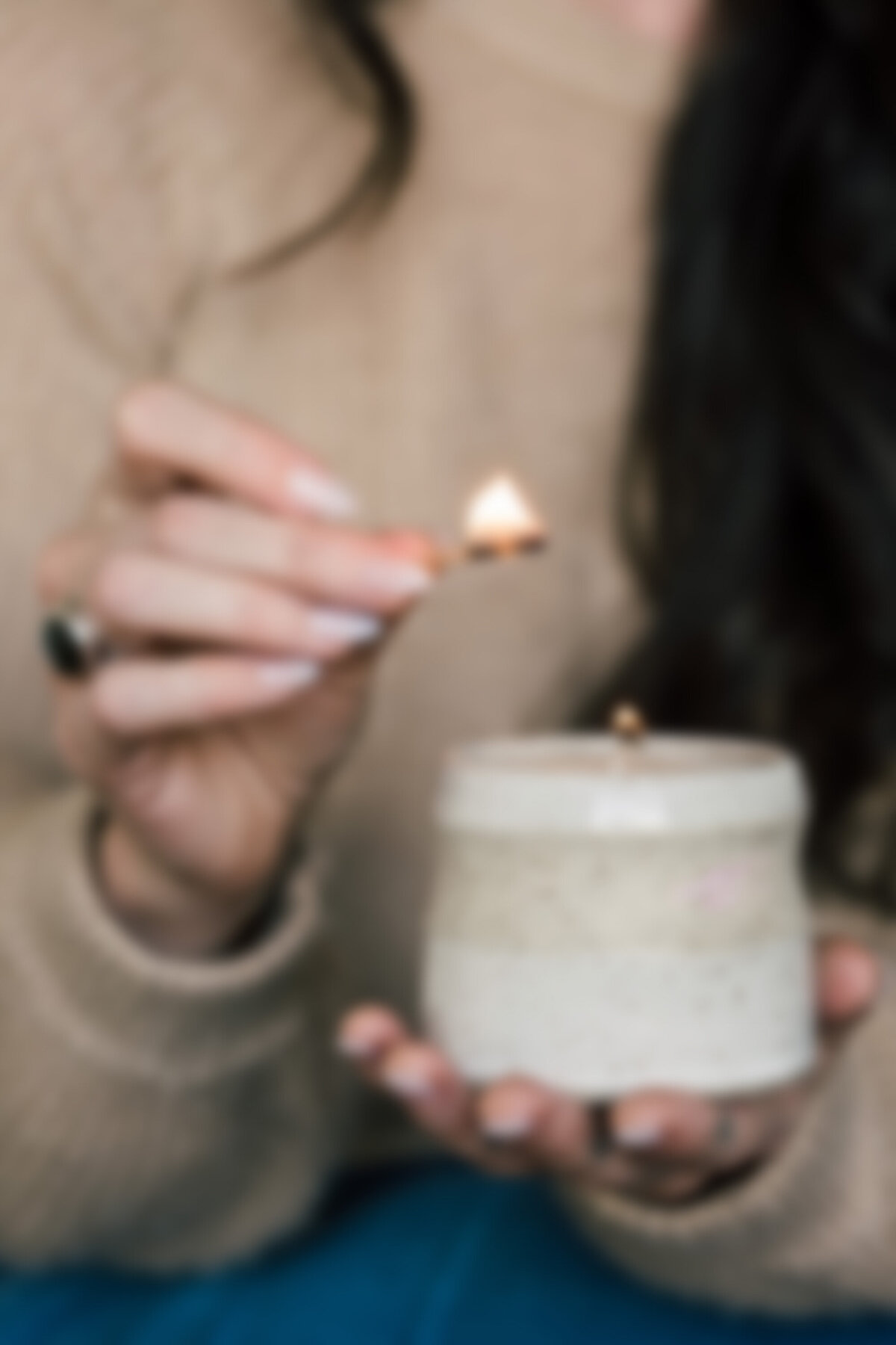 Blurry close-up of woman lighting a handmade ceramic candle with a match, symbolizing ritual, self-care, and slow living in a spiritual workspace