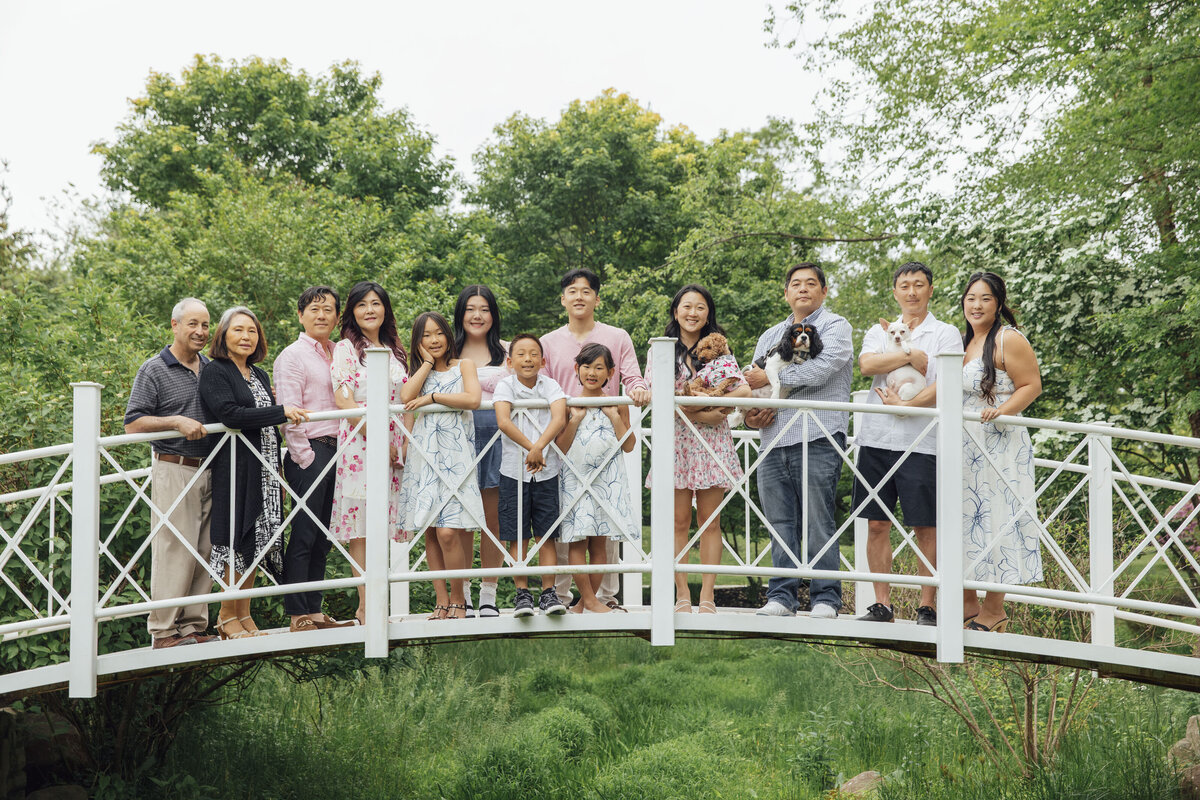 Family Portrait Photographer | Asian family posing together on the white bridge surrounded by greenery at Sayen Gardens | Hamilton, New Jersey