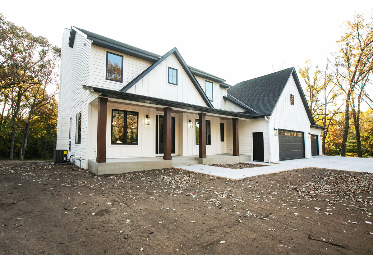 Exterior view of custom home in Big Lake Township, Minnesota with farmhouse details, cream siding, wood pillars and front porch built by Cornerstone Custom Builds