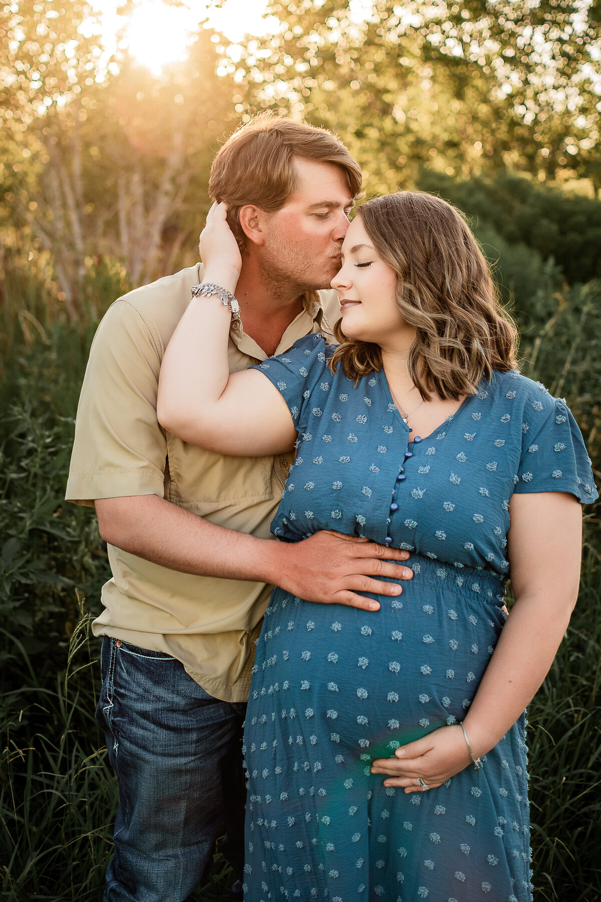 A mom to be pulls her husband in close as he kisses her forehead at their maternity session.