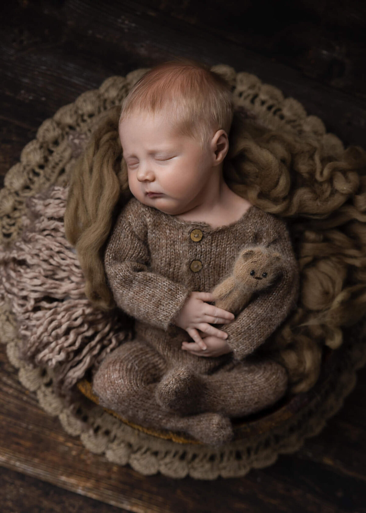 newborn baby laying in a wooden bowl holding a tiny teddy bear