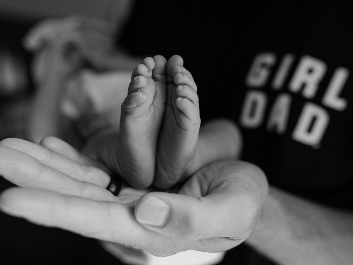 dad holding newborn baby girl showing feet for in home session