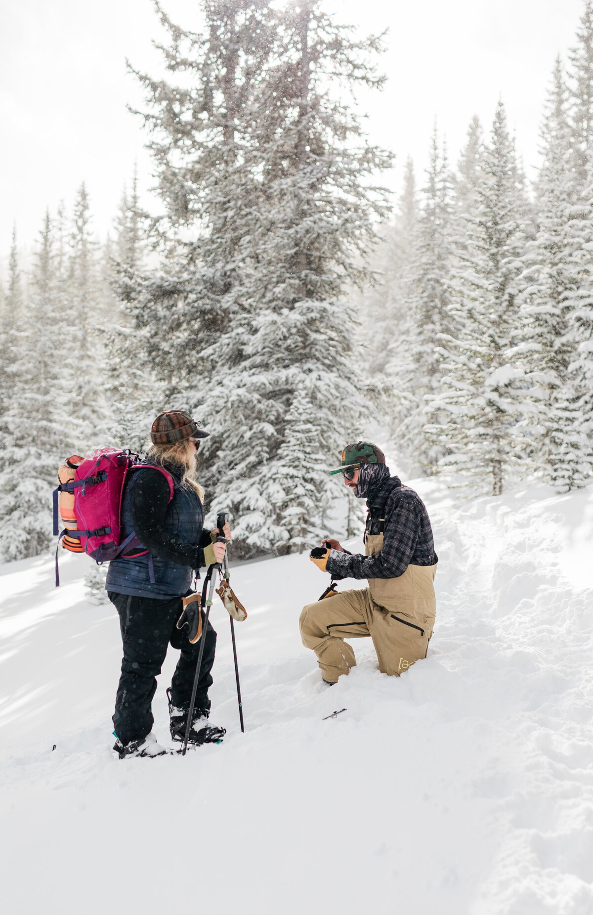 A couple in all snowboard gear in the backcountry are being photographed mid proposal