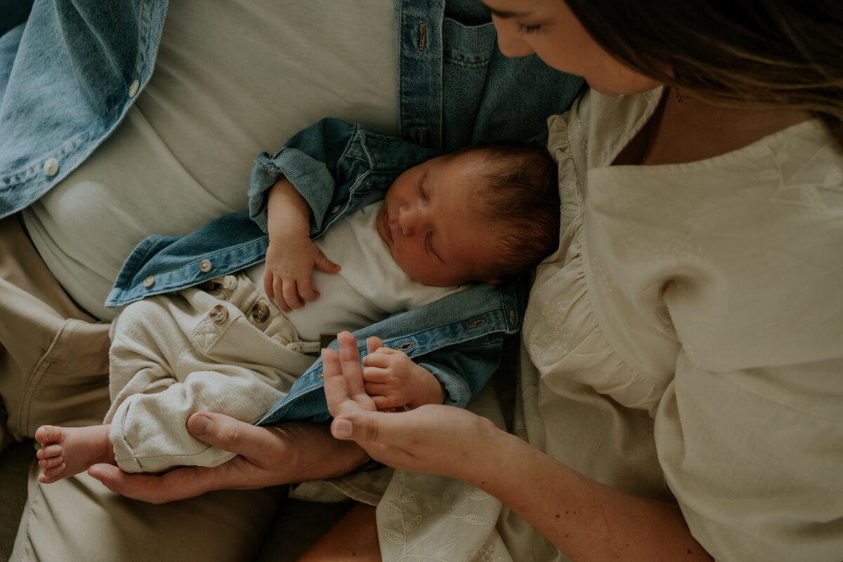 Newbornshoot aan huis te Asse, baby ligt heerlijk te slapen in de armen van de ouders.
