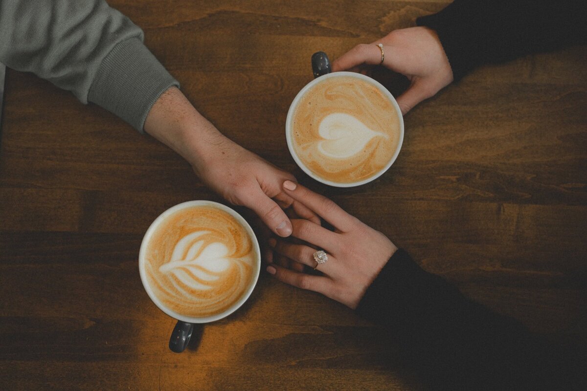 Engaged couple hold hands between two coffee cups at Analog Coffee in Calgary