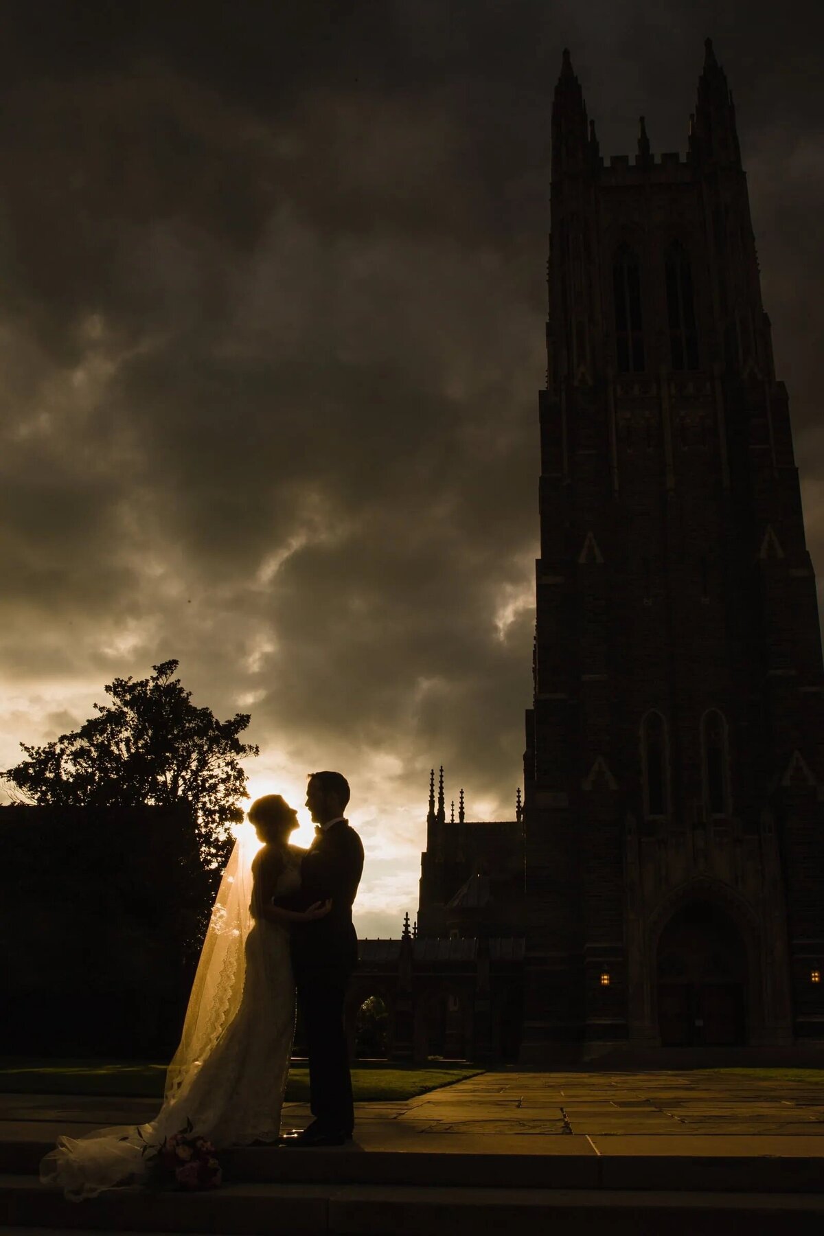 Silhouette of a bride and groom in front of the grand Duke Chapel at dusk, with the silhouette of the chapel accentuated against a cloudy sky