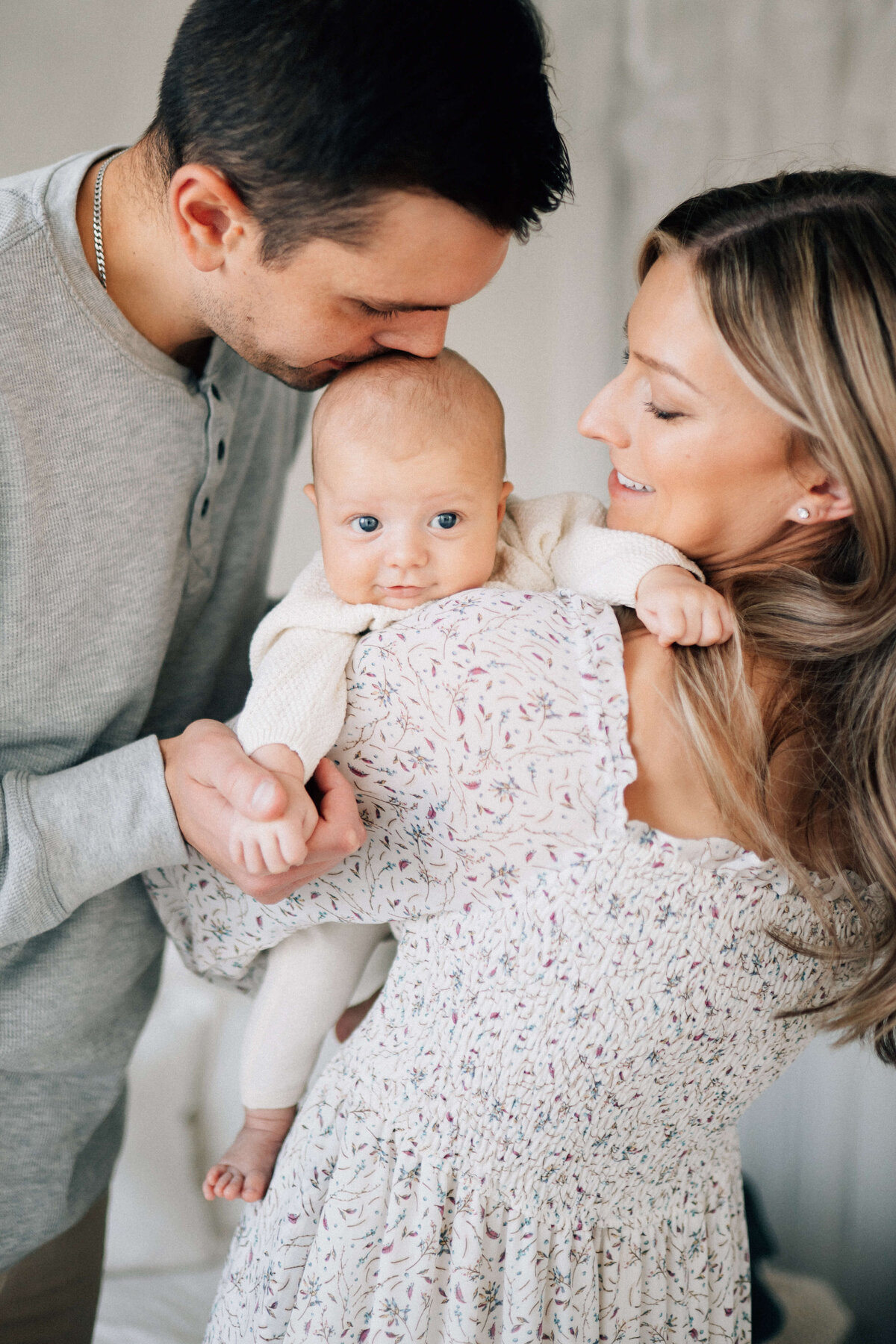 mom holding smiling baby boy over her shoulder while dad holds his hand and kisses his head