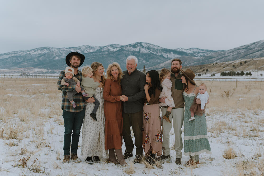 A family consisting of 7 adults and 4 young children smile for a family photo. Some are posed and looking at the camera and others are more candid, looking at each other.