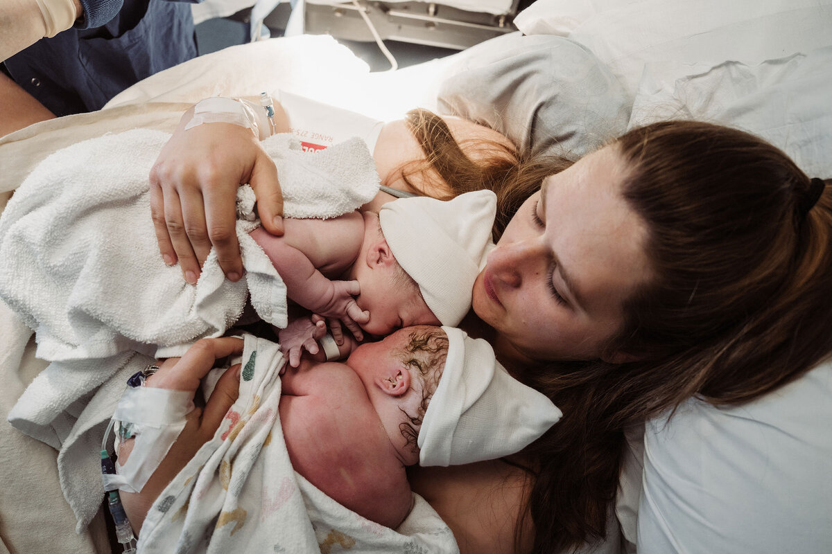 mother snuggles newborn and two daughters after home birth