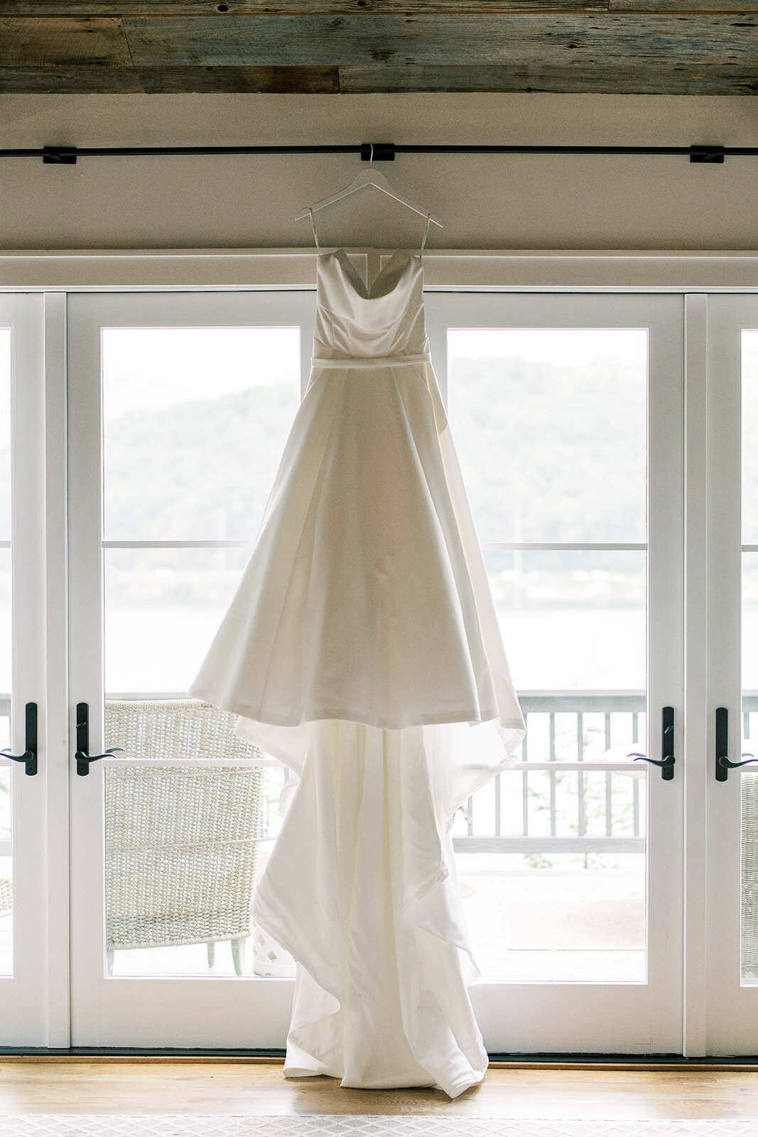 Wedding gown hanging in front of large windows overlooking the lake at a mountain rental home in Cashiers NC.