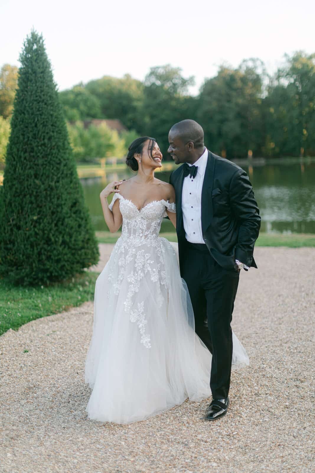 Joyful bride and groom walking together near a tranquil lake, captured by Paris wedding photographer Thomas Raboteur