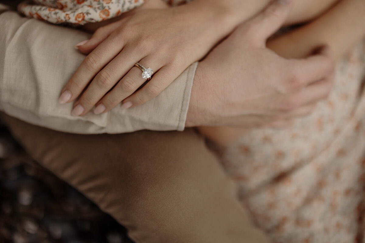 In a fine art wedding portrait, a couple's embrace speaks volumes. Her floral dress and diamond ring hint at engagement, while his beige shirt complements the tender mood. Captured by a skilled New England family photographer, this moment reflects their intimate journey together.