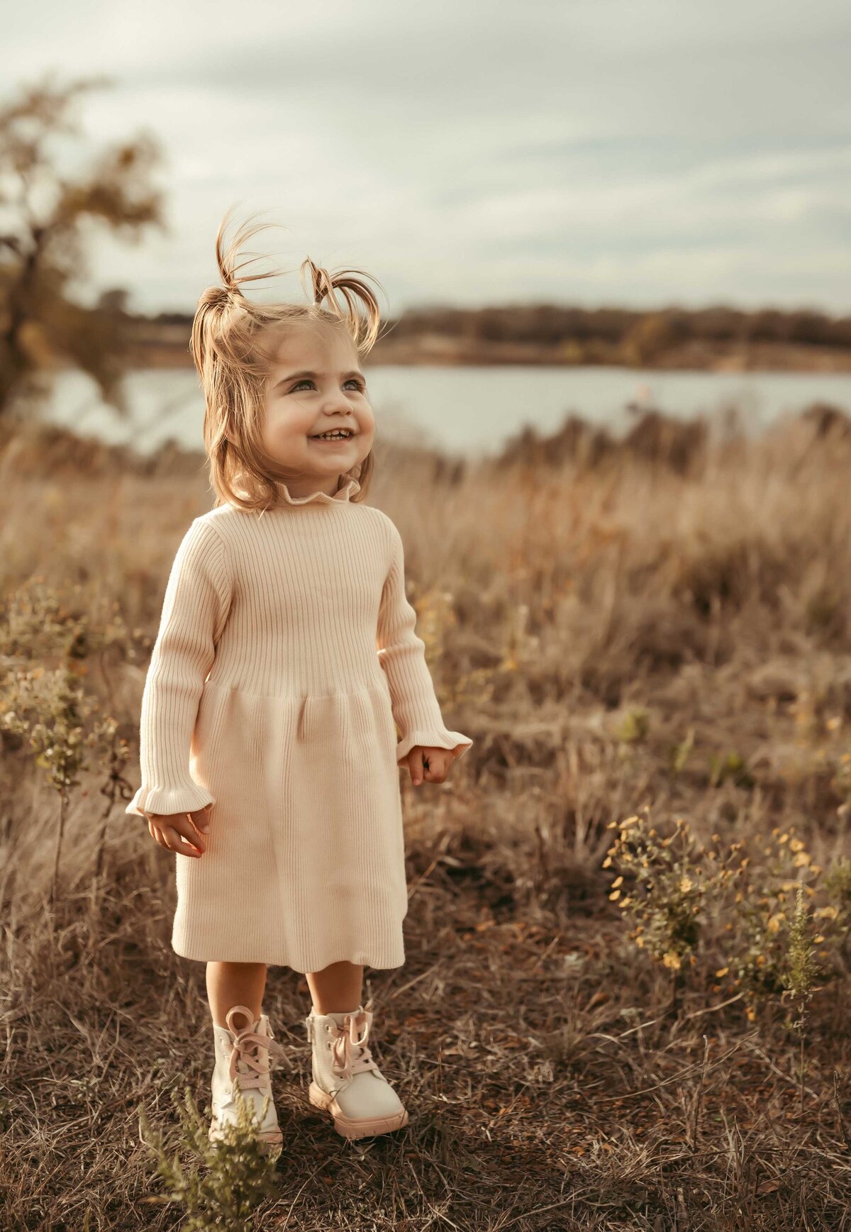 Little girl looking up at the sky smiling. She is wearing a soft pink knitted dress and white combat boots