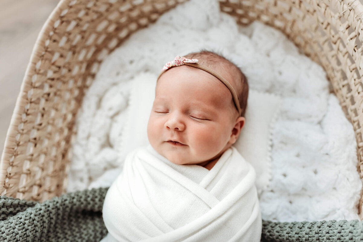 newborn girl wrapped in swaddle in moses basket