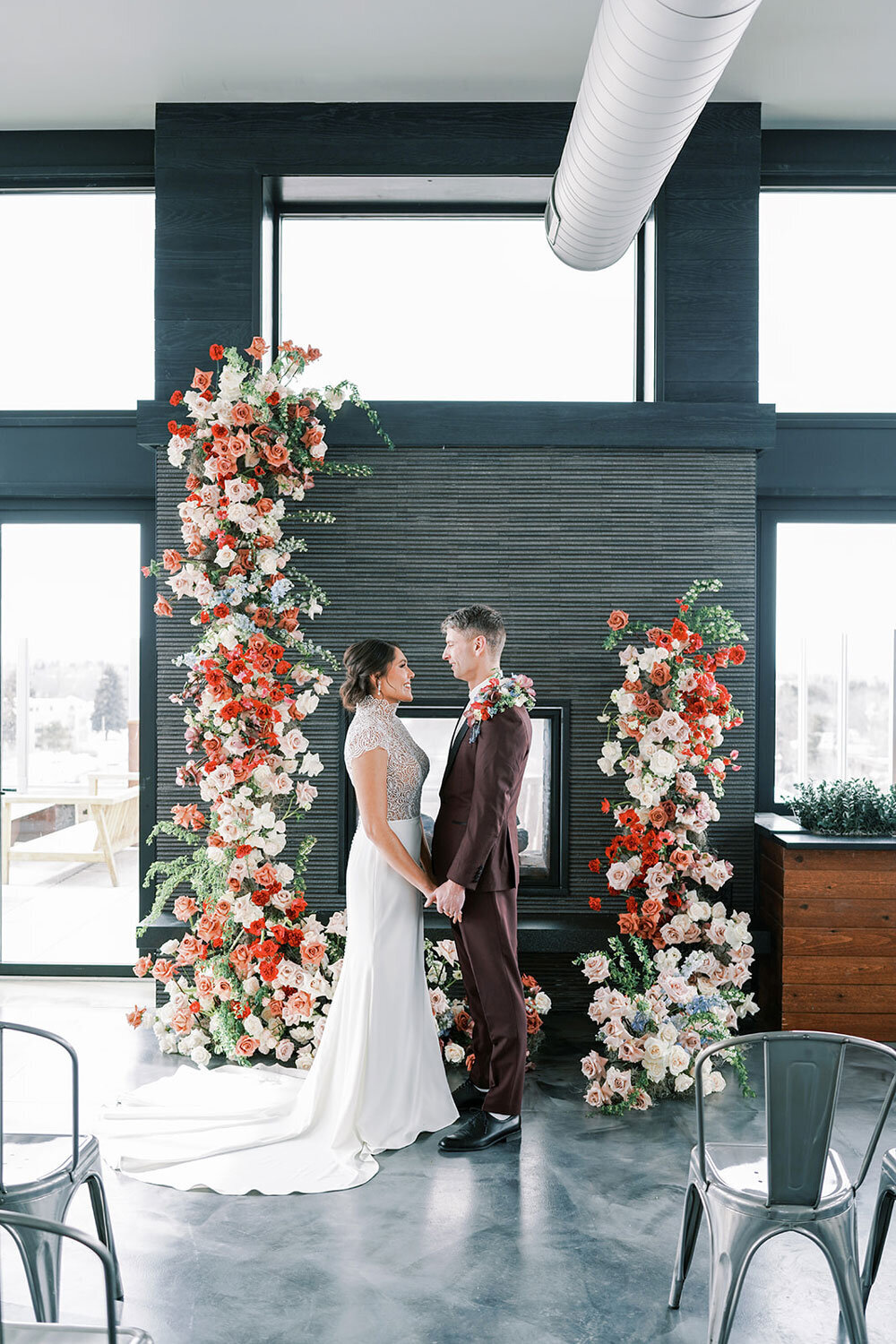 Bride and groom standing in front of a fireplace with coral, blush, and ivory floral pillars for a modern wedding inspiration shoot in Bozeman.