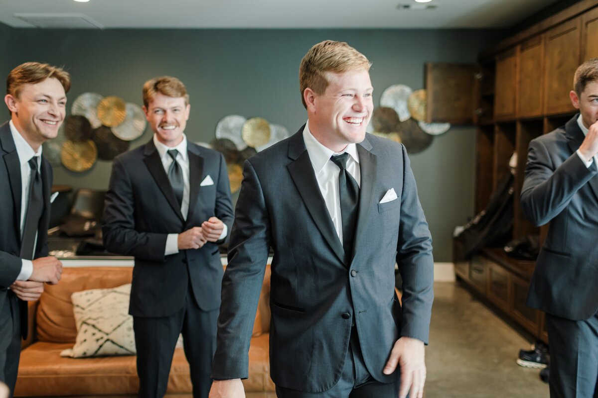 A moment captured by an Arkansas wedding photographer of a groom in a grey suit laughing with his groomsmen in the getting ready room