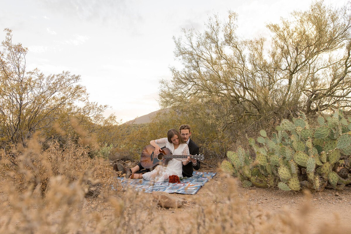 An eloping couple shares a quiet moment playing the guitar in the desert
