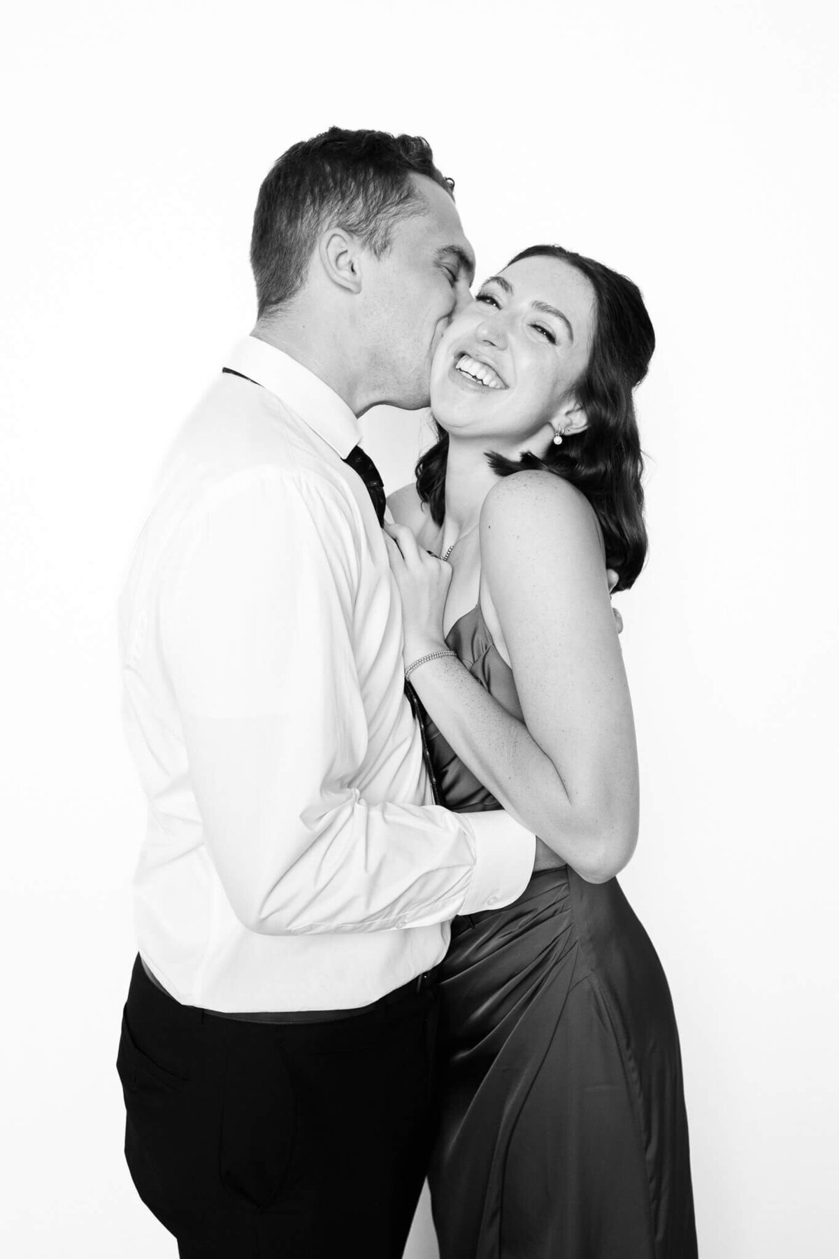 A candid moment of laughter as a man kisses his partner’s cheek, photographed in classic black and white by Monochrome Portraits, a Phoenix photo booth portrait experience.