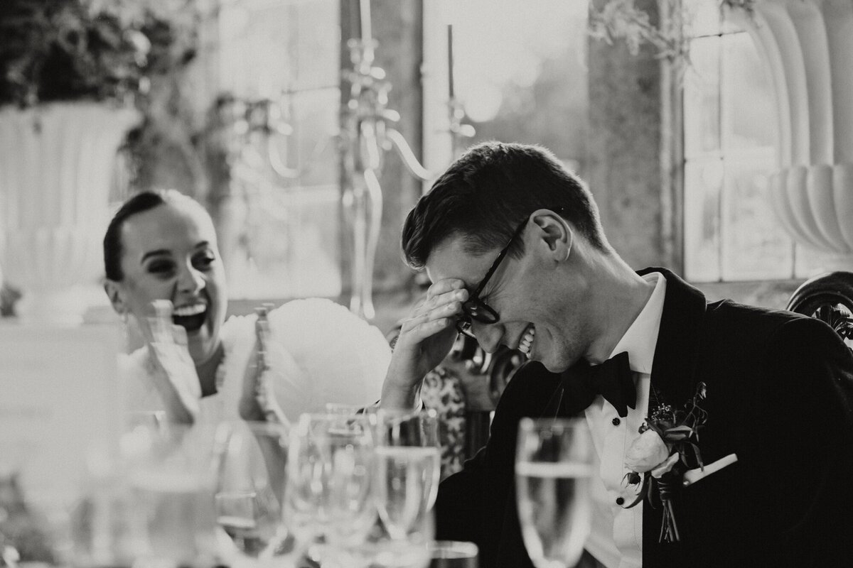 Black and white image of groom laighing at speeches 