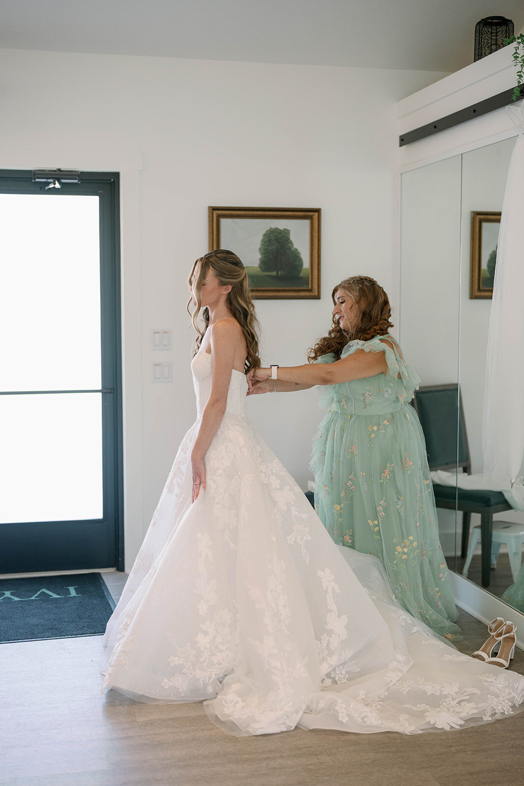 Emotional moment of the mother of the bride zipping up the wedding dress before the greenhouse ceremony at The Ivy House.