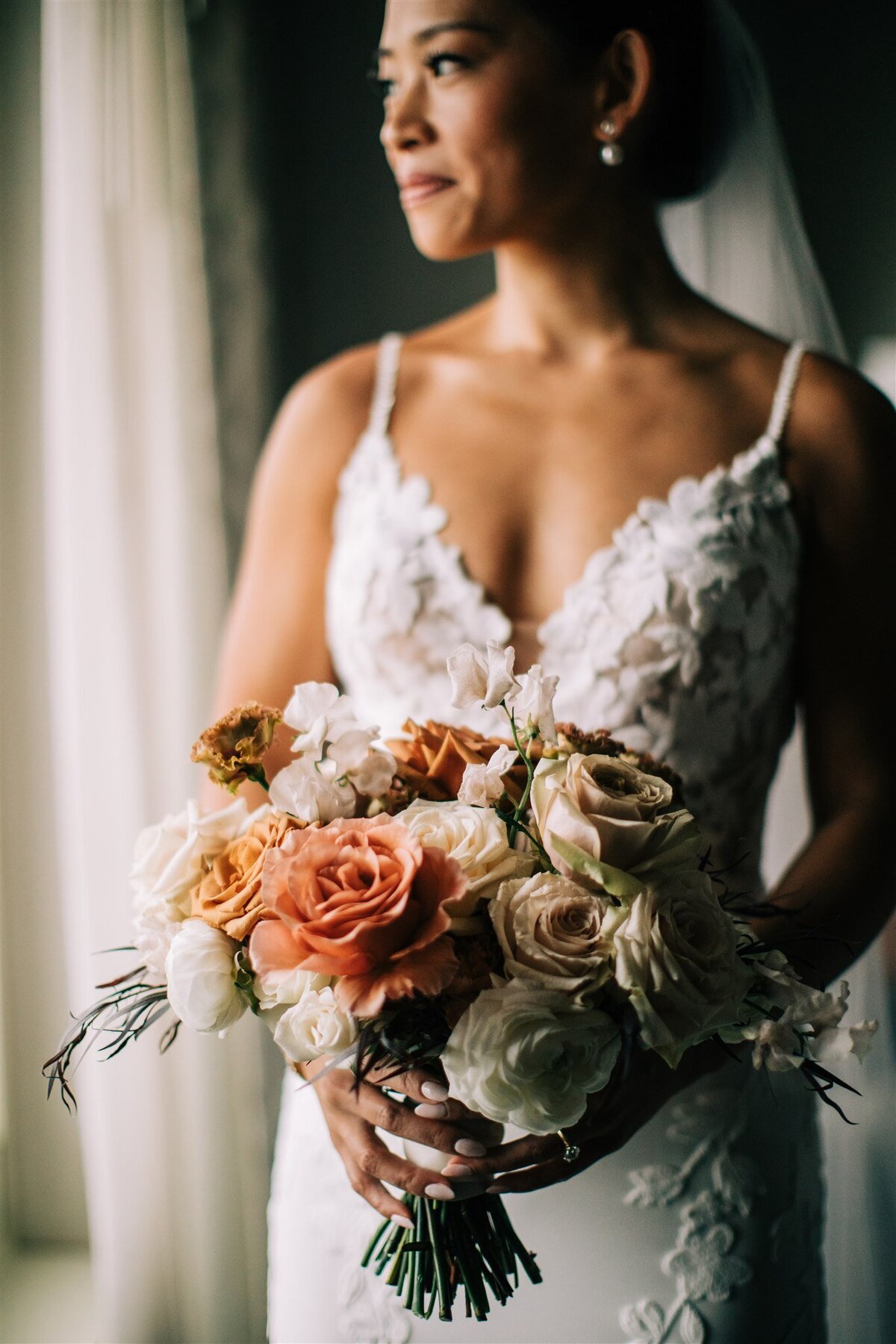 Romantic close-up of a bride in a lace wedding dress holding a bouquet of peach and blush flowers