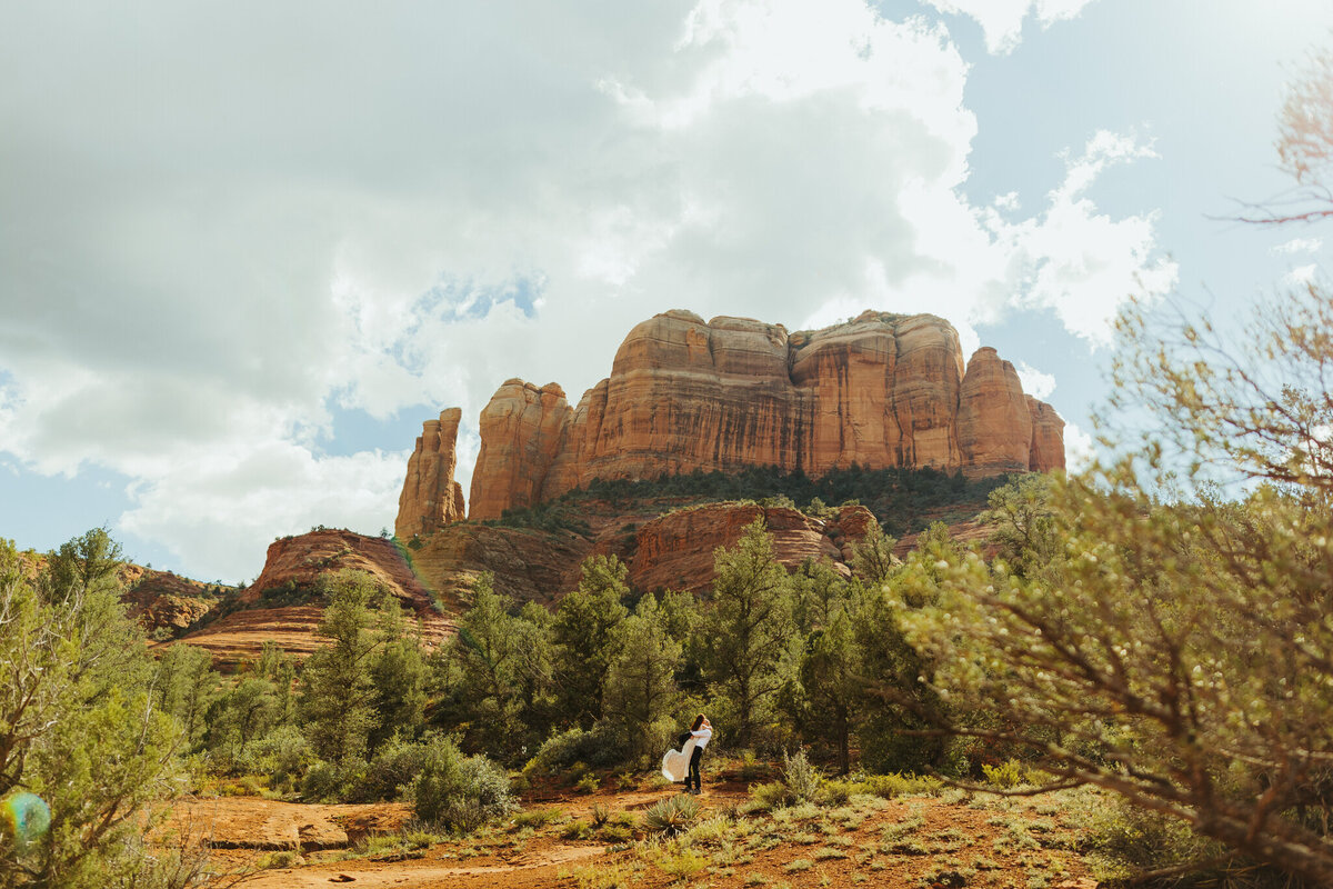 couple stands with towering catehdral rock in sedona behind them
