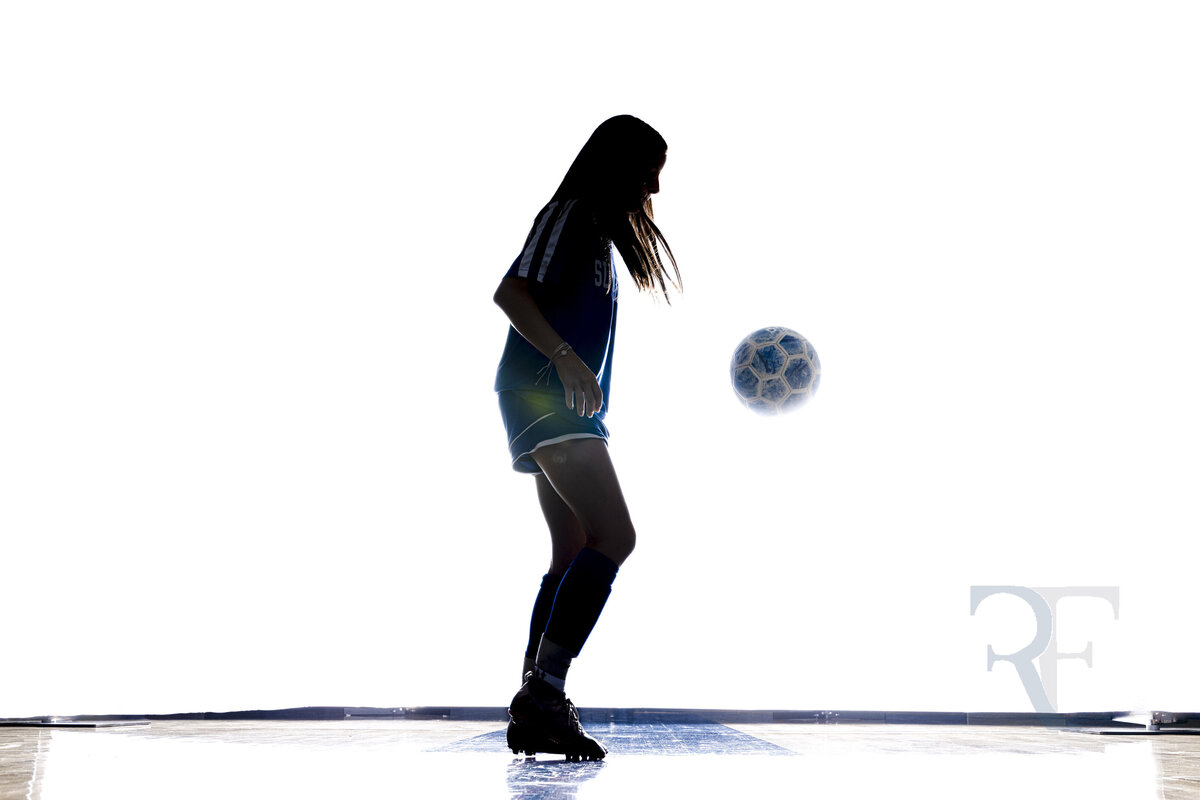 Photographer in Avon | Rob Faber Photography | Silhouette of a female soccer player juggling a ball mid-air, captured in dramatic backlighting.