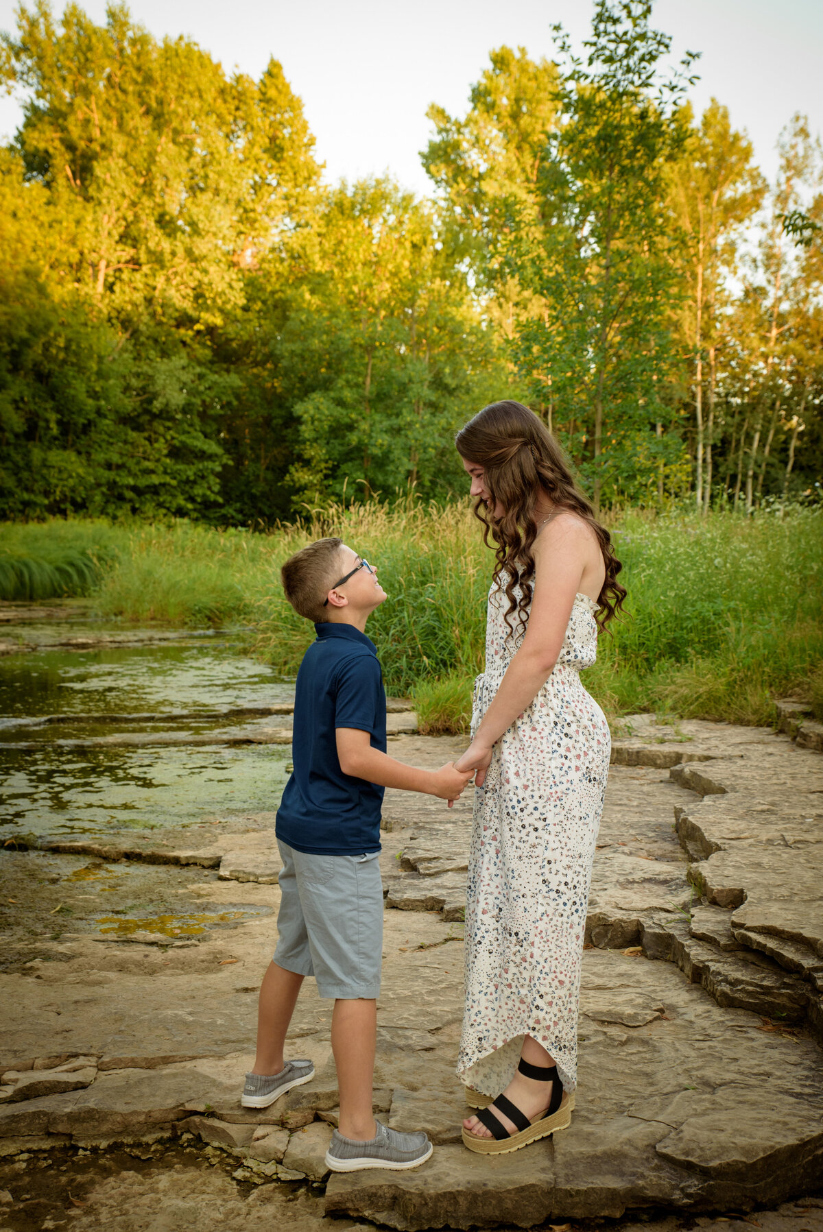 Sibling portrait with brother and sister looking at each other holding hands near the creek at Fonferek Glen County Park near Green Bay, Wisconsin