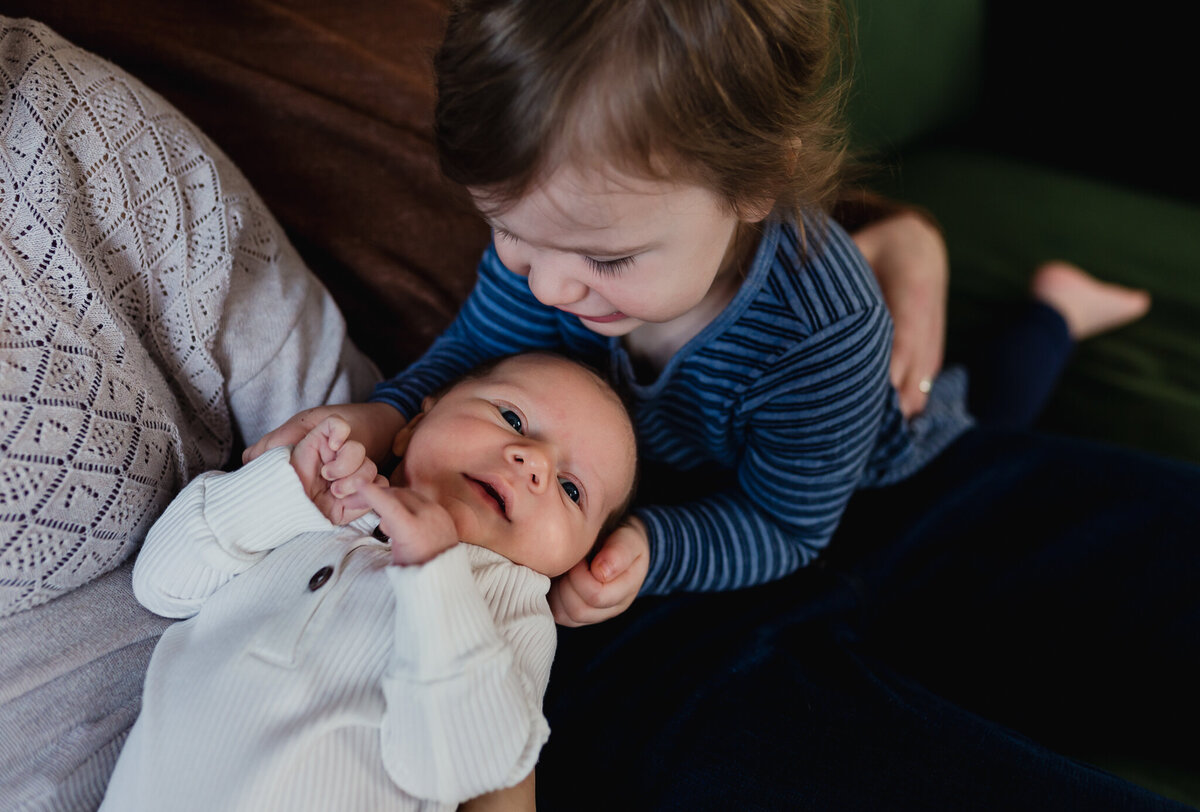 Newborn baby being held by mom with younger sibling holding head.