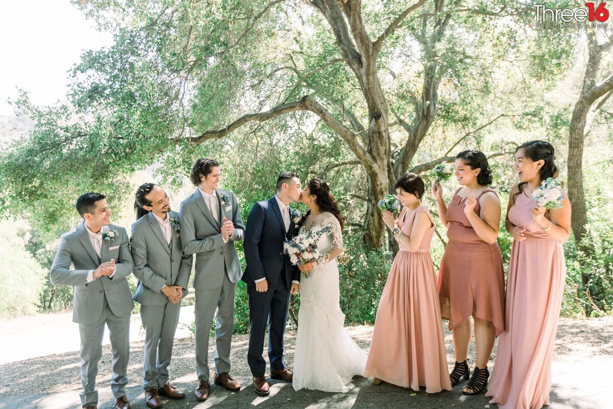 Bride and Groom share a kiss as the wedding party looks on