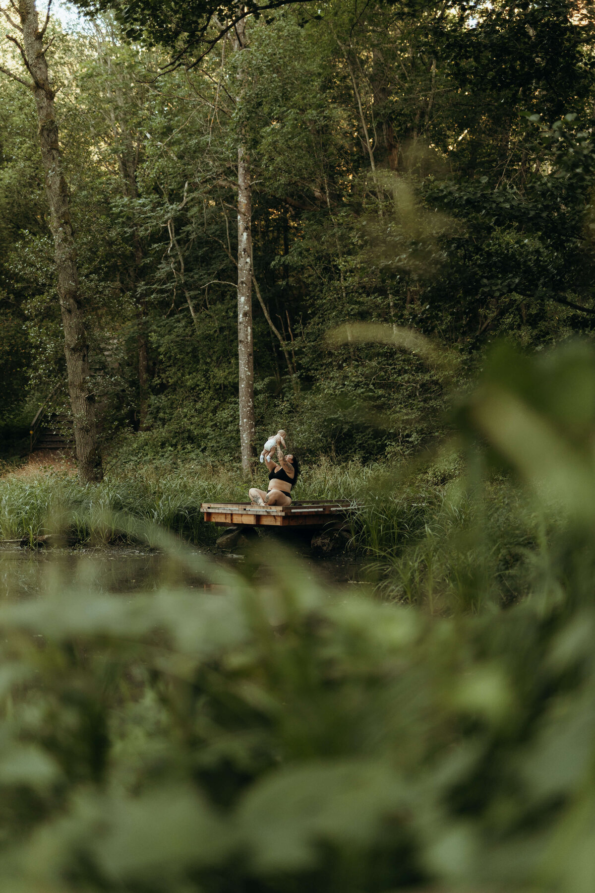 En bild på en mamma med sin son sittandes på en brygga vid en damm i grön natur i Stockholm