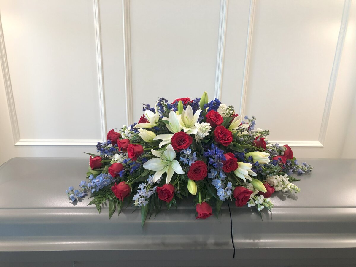 red roses white lilies and blue delphinium funeral casket flowers at White Pine Funeral Flowers
