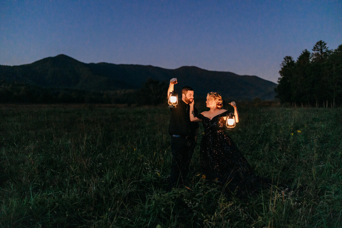 Couple hold lanterns while wearing all black as night takes over mountains