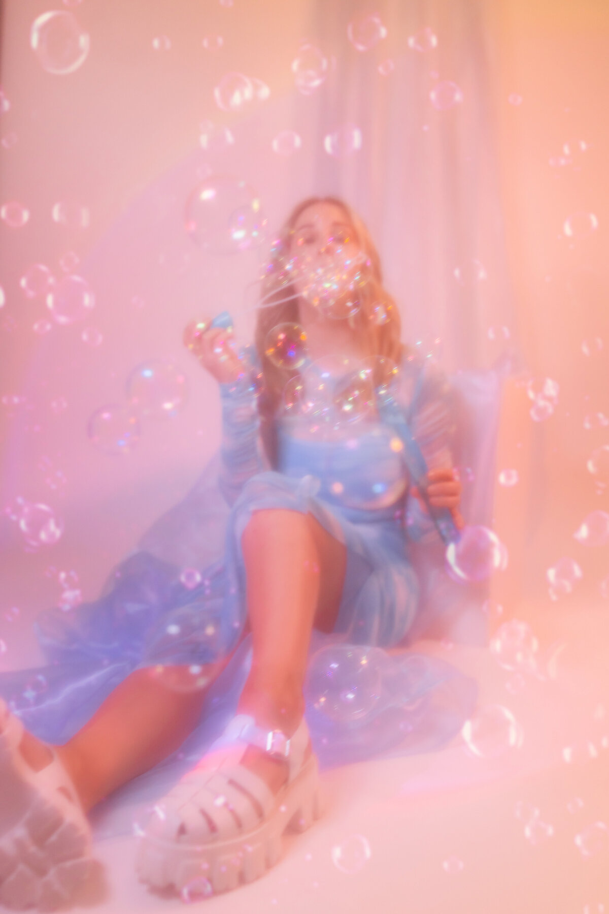 Soft, dreamy editorial-style portrait of a woman blowing bubbles in a flowy blue dress, surrounded by pastel tones. Shot in Greenville SC by Dani Lacey.