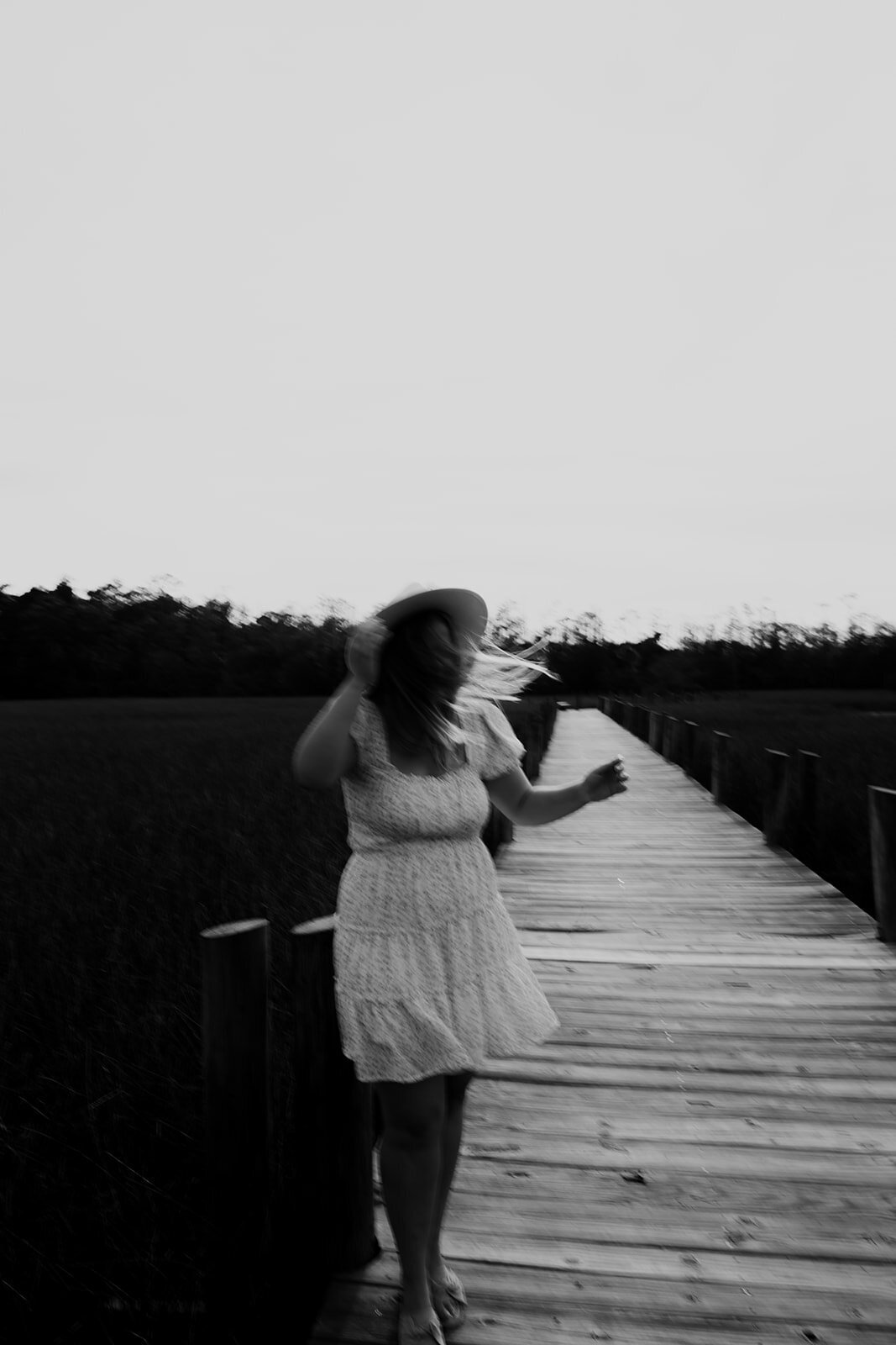 Artsy black and white photo of woman twirling on wooden boardwalk. Slight motion blurr.