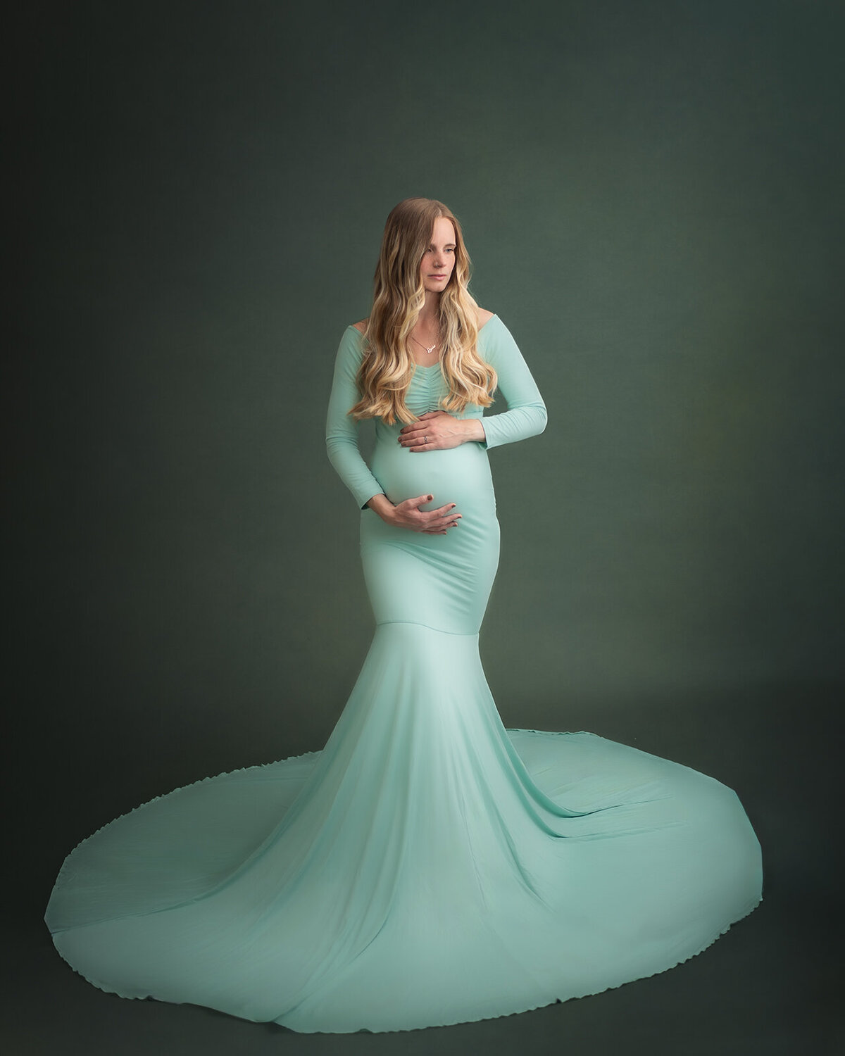 pregnant woman in seafoam dress holding belly and looking to side