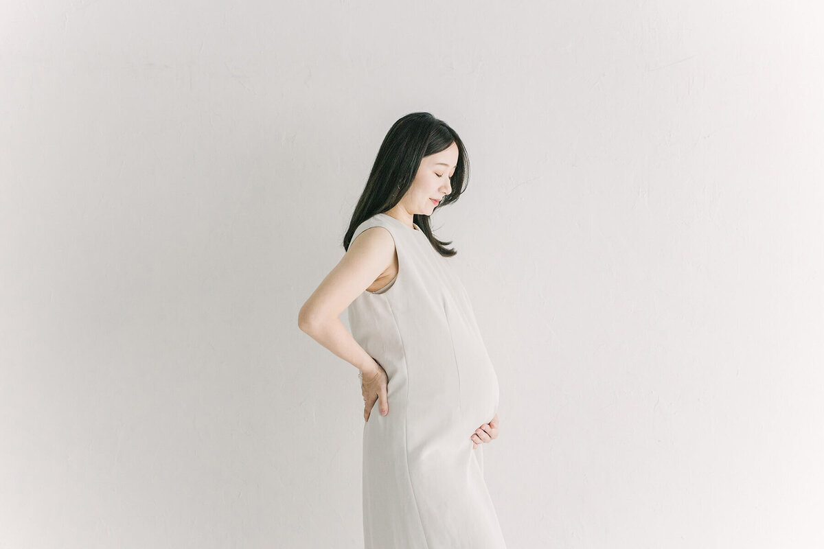 ホワイトコーデでおなかが引き立つ美しくおしゃれなマタニティフォト。妊婦さんのママはおなかを眺めて笑っています。