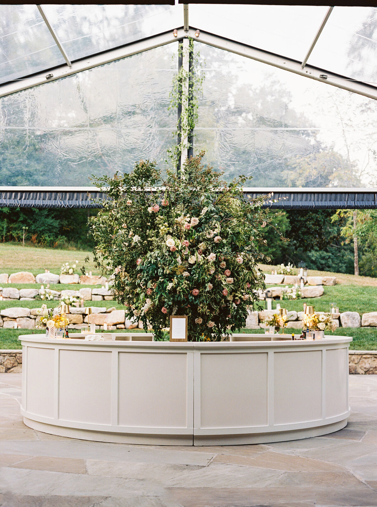 Lush garden inspired floral design growing in Bramble at Blackberry Farm for fall wedding reception. Growing floral installations on chandeliers and ceiling beams create garden setting for fall wedding reception. Timeless and elegant floral design in hues of white, cream, blush, and natural greens. Large trees with floral moments for outdoor wedding reception. Destination wedding at Blackberry Farm. Design by Rosemary & Finch Floral Design in Nashville, TN.