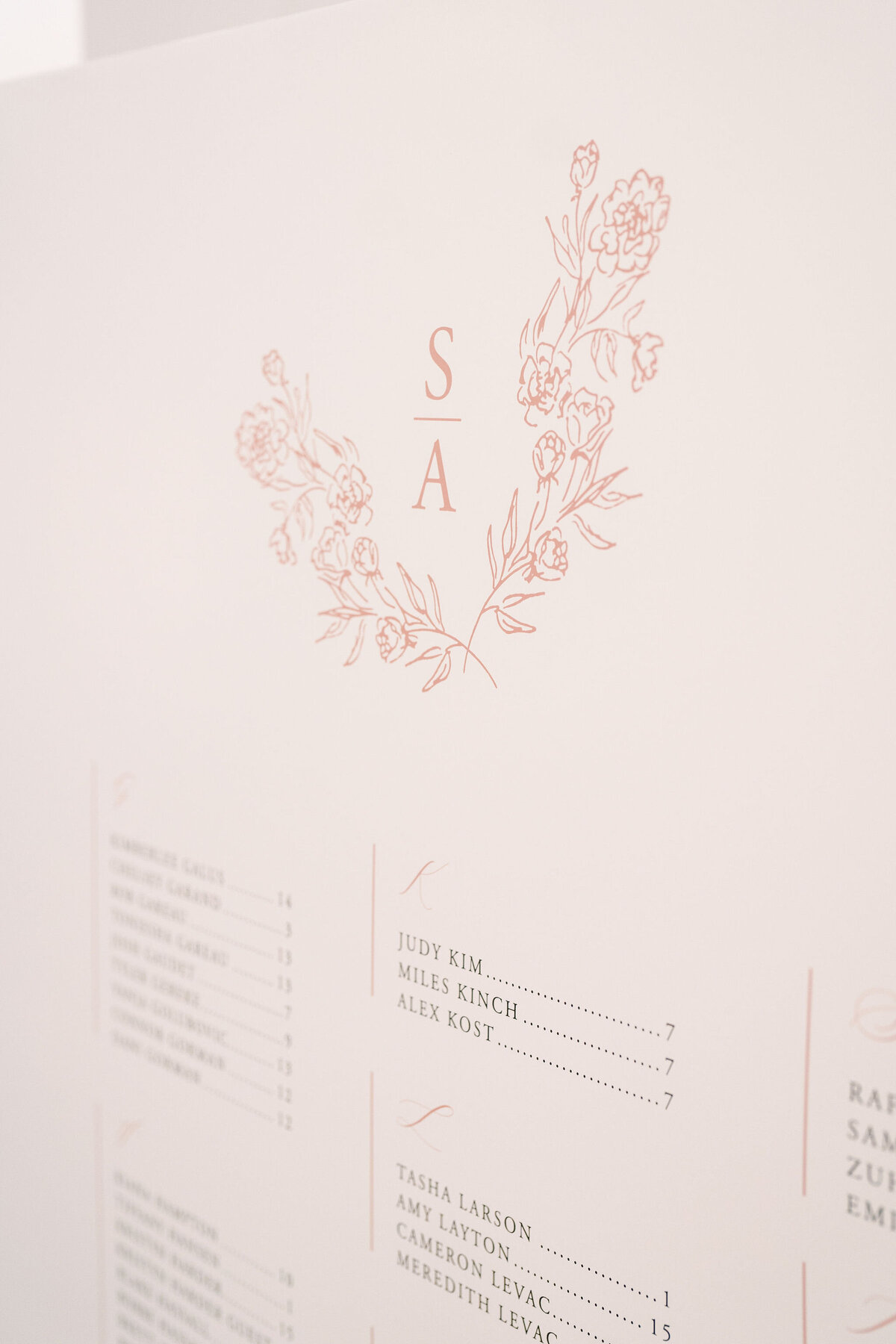 A seating chart for a modern &amp; romantic wedding in Calgary, adorned with floral illustrations and the initials "S A" at the top. It lists names such as Judy Kim, Amy Layton, and others, along with their respective table numbers.