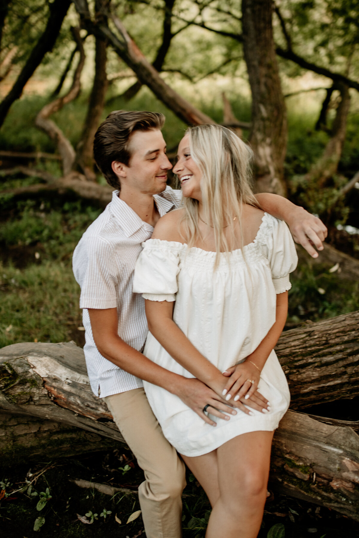 Wisconsin couple cuddles up on a tree in the forest during a Minnesota engagement photoshoot, captured by Emmie Verdell Photo.