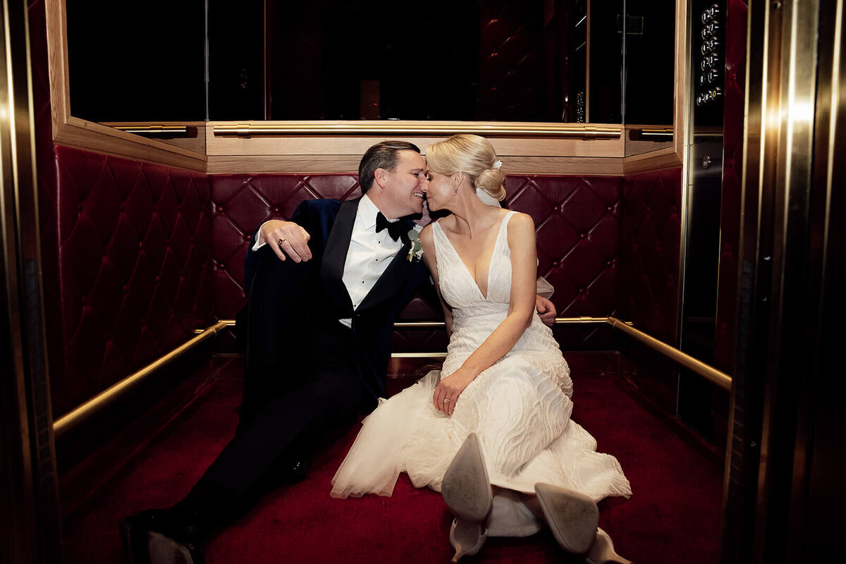 couple sat on the floor kissing in a lift with a red carpet and red leather walls