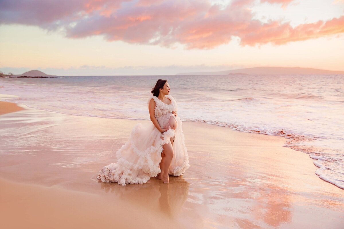 Woman stands in reflective pool and photographed at sunset while babymooning on Maui