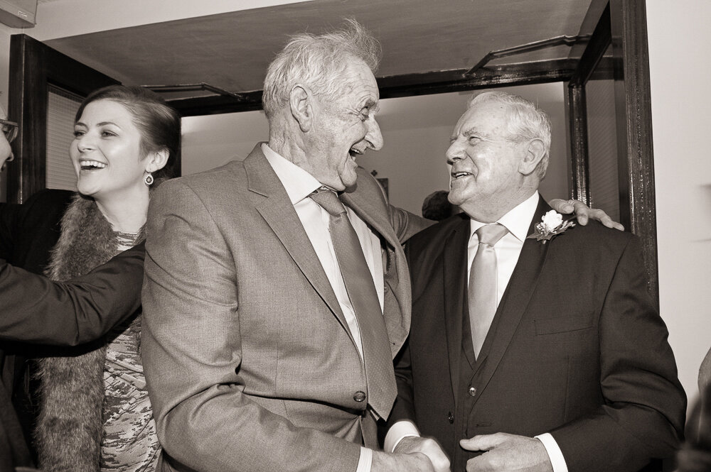 two elderly men embracing and laughing together outside Curaheen church