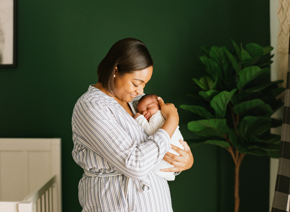 Mom holding her newborn son in his emerald green nursery during a newborn session photographed in Raleigh. Photographed by newborn photographers Raleigh A.J. Dunlap Photography.
