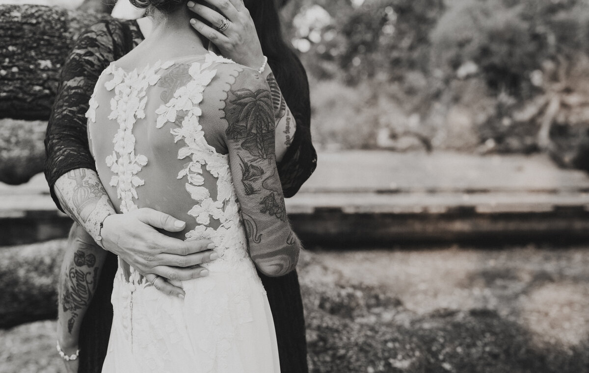 Close-up black and white image of tattooed brides holding each other, showing intricate ink and lace details during Florida elopement.